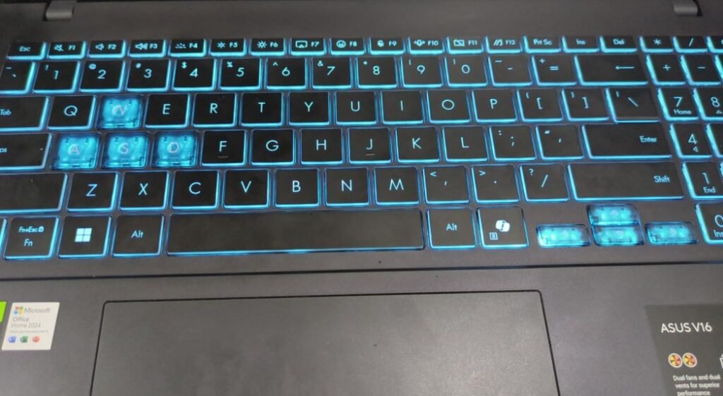 ASUS V16 laptop keyboard with cyan backlight and highlighted WASD keys